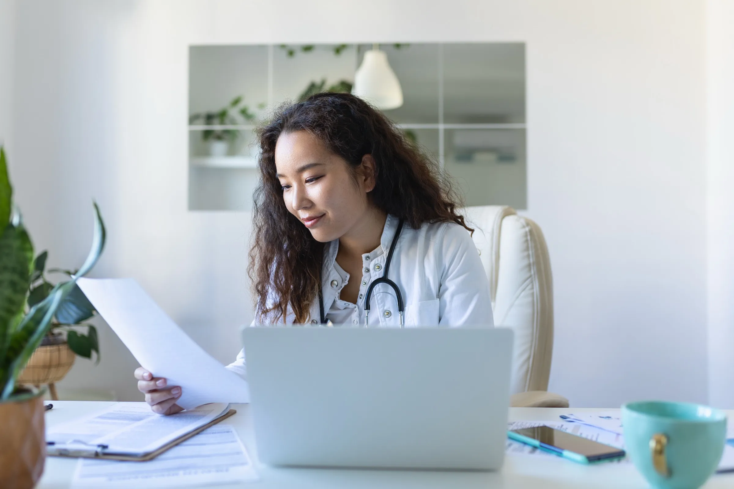 Clinician reviewing documentation at a laptop in a bright medical workspace.